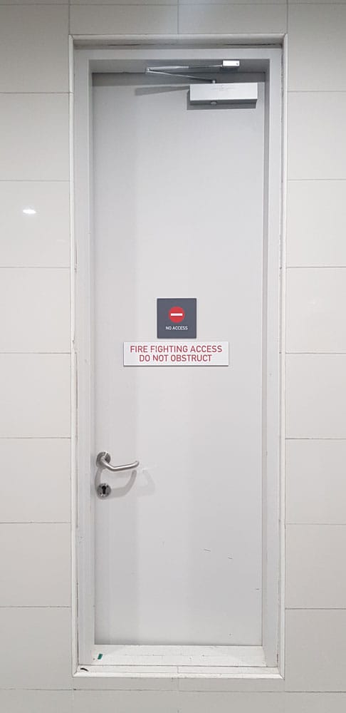 White steel door with lever handle marked Fire Fighting Access - Do Not Obstruct