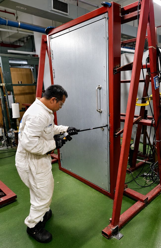 Technician testing a forced entry steel door mounted in a steel test rig
