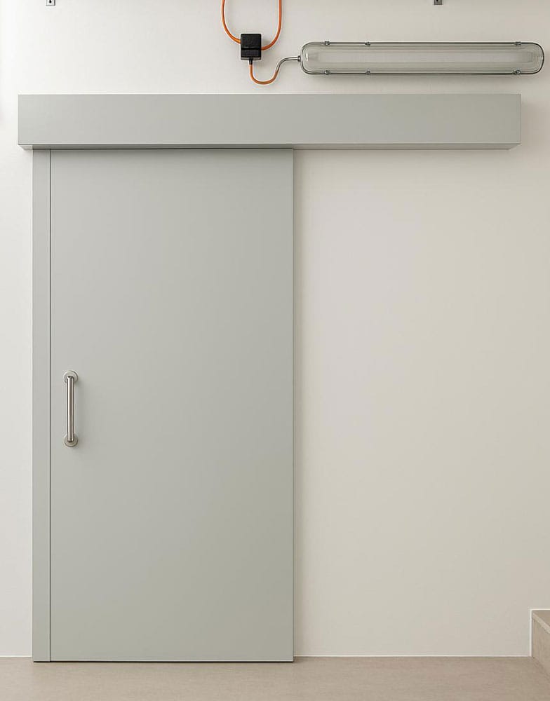 Pale grey sliding fire steel door with pull handle on an overhead track