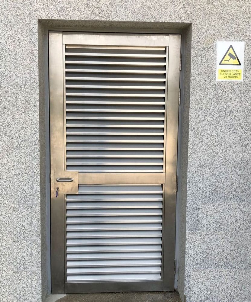 Louvred stainless steel door with padlock hasp in a textured concrete wall