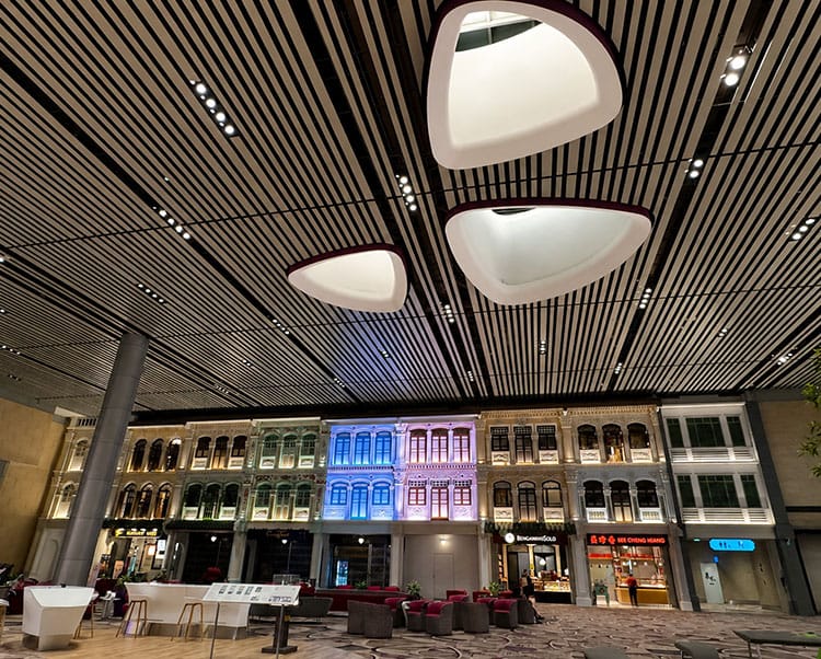 Airport terminal interior with pod-shaped ceiling lights and shophouse-style storefronts